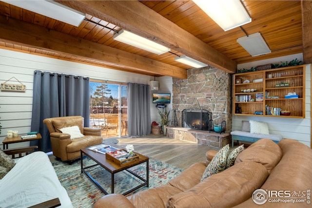 living area with wood ceiling, beamed ceiling, wood finished floors, a stone fireplace, and wood walls