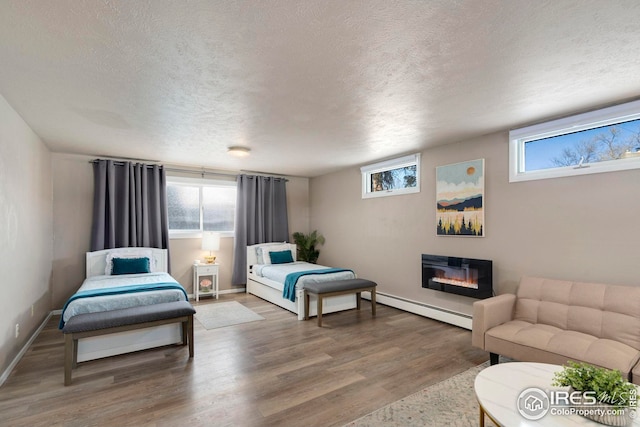 bedroom featuring multiple windows, a baseboard heating unit, wood finished floors, and a glass covered fireplace