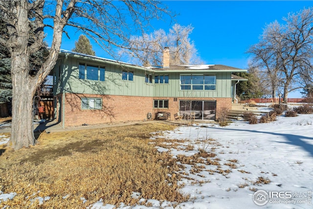 snow covered property with a chimney and brick siding