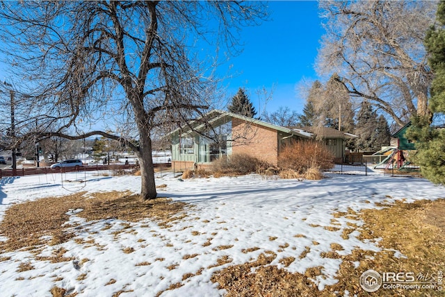 view of snow covered exterior with a playground and brick siding