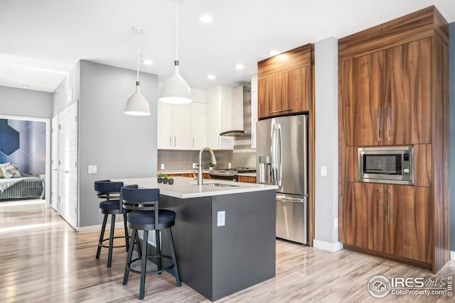 kitchen featuring white cabinetry, pendant lighting, stainless steel appliances, a kitchen island with sink, and wall chimney range hood