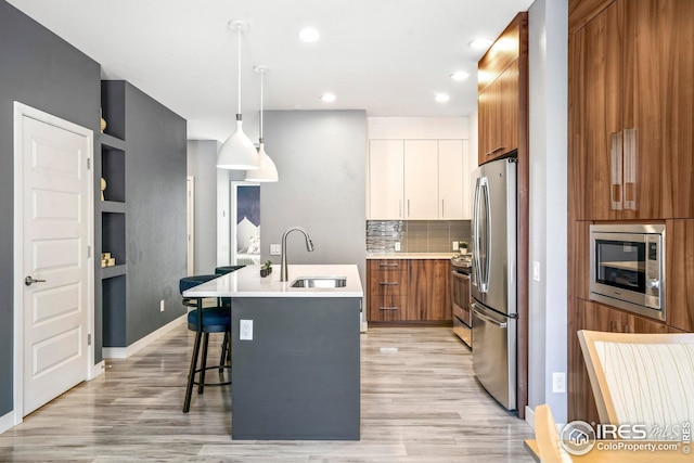 kitchen with appliances with stainless steel finishes, white cabinetry, an island with sink, sink, and hanging light fixtures