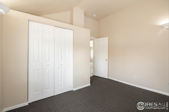 unfurnished bedroom with lofted ceiling, dark carpet, and a closet