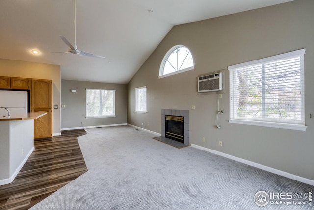 unfurnished living room featuring ceiling fan, a tiled fireplace, high vaulted ceiling, and an AC wall unit