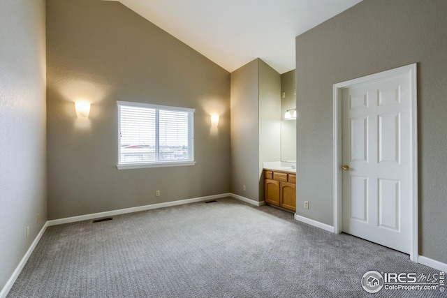 interior space with ensuite bath, high vaulted ceiling, and light carpet