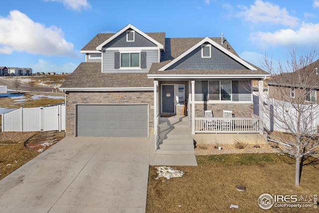 view of front of property with a shingled roof, covered porch, an attached garage, stone siding, and driveway