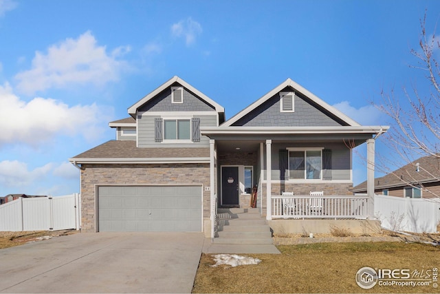 craftsman-style home featuring covered porch, a garage, fence, stone siding, and concrete driveway