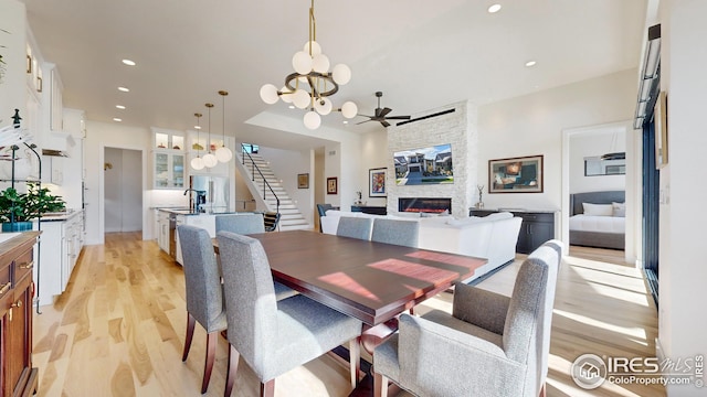 dining area with stairway, light wood-type flooring, a fireplace, a notable chandelier, and recessed lighting