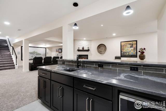 kitchen featuring decorative light fixtures, a fireplace, open floor plan, a sink, and dark cabinetry