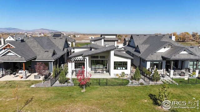 rear view of house with a patio, a fenced backyard, a tiled roof, a yard, and a mountain view