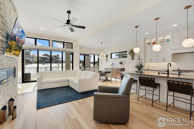 living room with a water view, light wood-style floors, ceiling fan with notable chandelier, and a stone fireplace