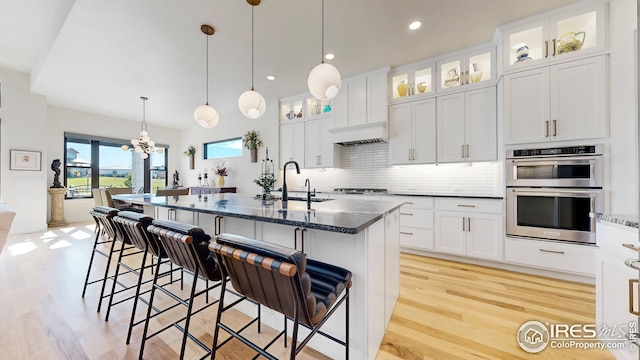 kitchen featuring glass insert cabinets, a kitchen island with sink, a sink, and dark stone countertops