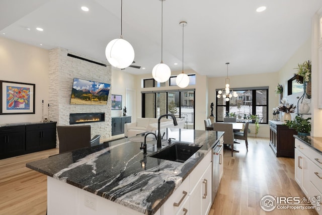 kitchen featuring pendant lighting, white cabinets, a sink, dark stone countertops, and an island with sink