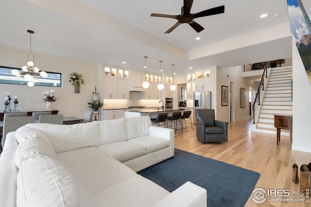 living area with light wood-style flooring, recessed lighting, ceiling fan with notable chandelier, baseboards, and stairway