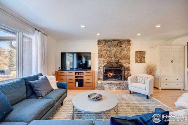 living room with ornamental molding, a stone fireplace, and light hardwood / wood-style floors