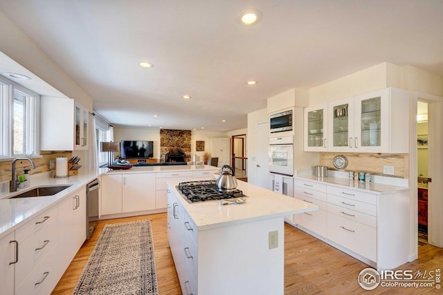 kitchen with sink, white cabinetry, light wood-type flooring, a kitchen island, and stainless steel appliances