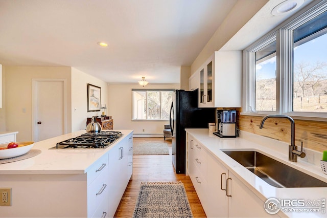 kitchen with stainless steel gas cooktop, sink, light hardwood / wood-style flooring, baseboard heating, and white cabinets