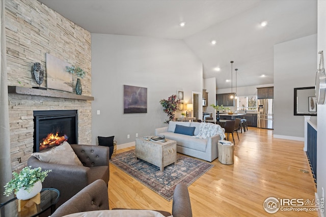 living room with high vaulted ceiling, a stone fireplace, and light hardwood / wood-style floors