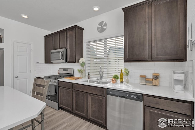 kitchen featuring a sink, light countertops, dark brown cabinets, light wood-style floors, and appliances with stainless steel finishes