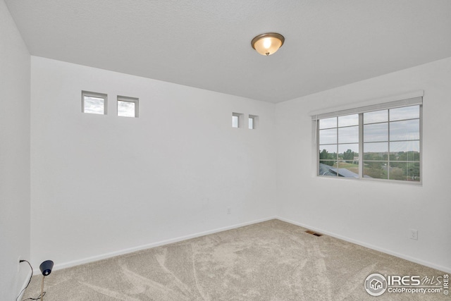 carpeted spare room featuring visible vents, baseboards, and a healthy amount of sunlight