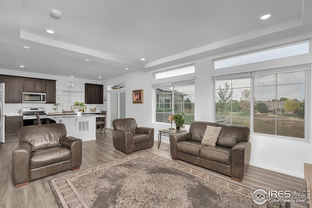 living room with recessed lighting, a tray ceiling, baseboards, and wood finished floors