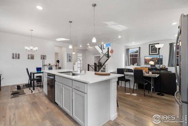 kitchen with sink, hanging light fixtures, an island with sink, stainless steel appliances, and hardwood / wood-style floors