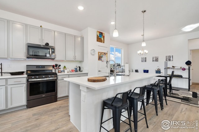 kitchen with appliances with stainless steel finishes, pendant lighting, an island with sink, a kitchen breakfast bar, and light wood-type flooring