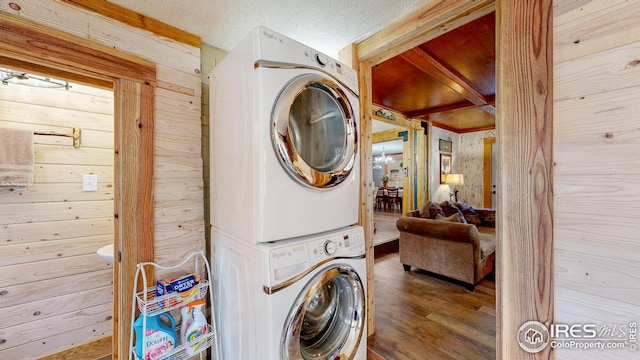 laundry area featuring wood-type flooring, stacked washer and clothes dryer, a textured ceiling, and wood walls