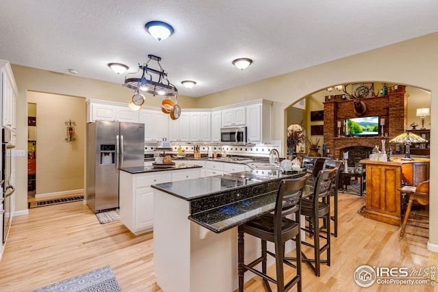 kitchen with appliances with stainless steel finishes, a breakfast bar, a fireplace, white cabinetry, and sink