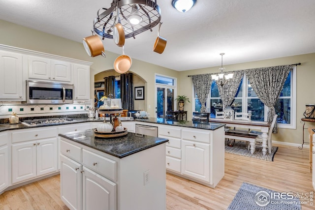 kitchen with pendant lighting, white cabinetry, stainless steel appliances, a kitchen island, and a chandelier