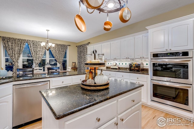 kitchen featuring a kitchen island, white cabinets, hanging light fixtures, stainless steel appliances, and light wood-type flooring