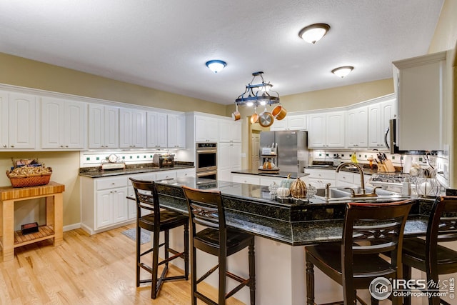 kitchen featuring a breakfast bar, sink, white cabinetry, light hardwood / wood-style flooring, and appliances with stainless steel finishes