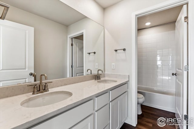 full bathroom featuring hardwood / wood-style flooring, tiled shower / bath, vanity, and toilet