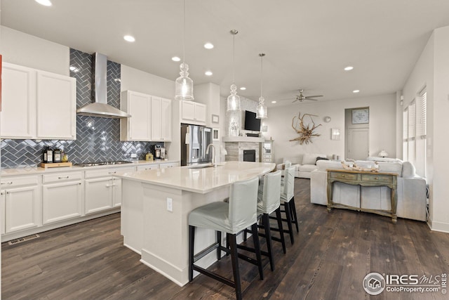 kitchen with white cabinets, decorative light fixtures, an island with sink, and wall chimney range hood