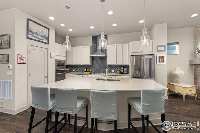 kitchen featuring wall chimney exhaust hood, white cabinetry, appliances with stainless steel finishes, and sink