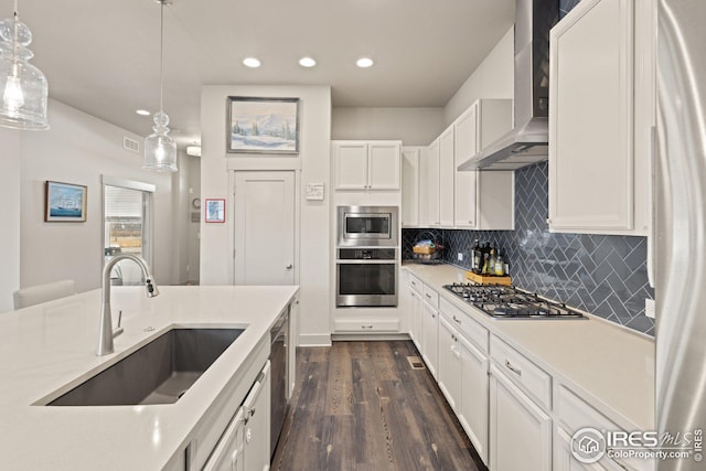 kitchen featuring decorative light fixtures, white cabinetry, sink, stainless steel appliances, and wall chimney range hood