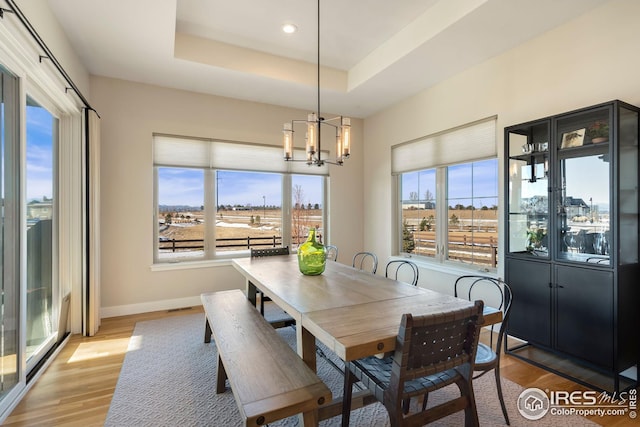 dining area with baseboards, a tray ceiling, light wood-style flooring, and a notable chandelier