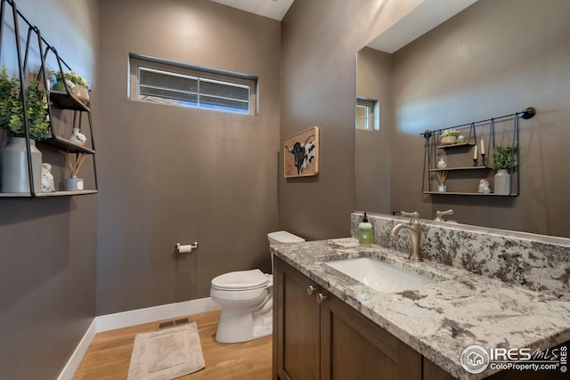 bathroom with vanity, toilet, baseboards, wood finished floors, and visible vents