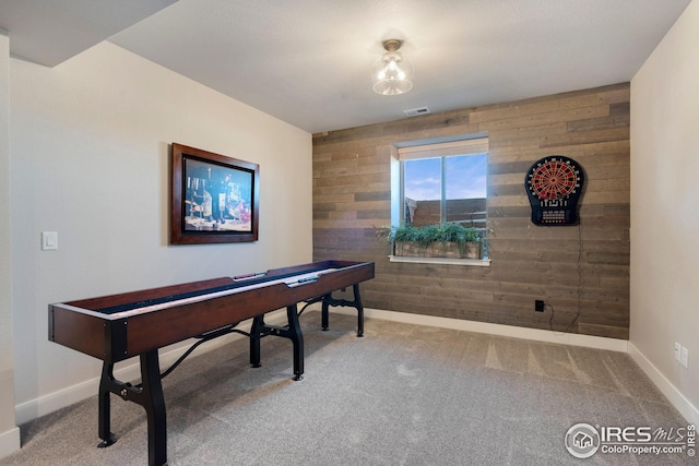 recreation room with baseboards, wood walls, and carpet
