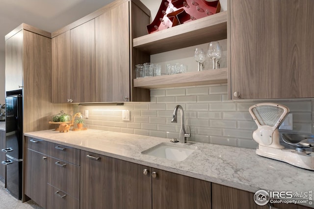 kitchen featuring backsplash, modern cabinets, open shelves, a sink, and light stone counters