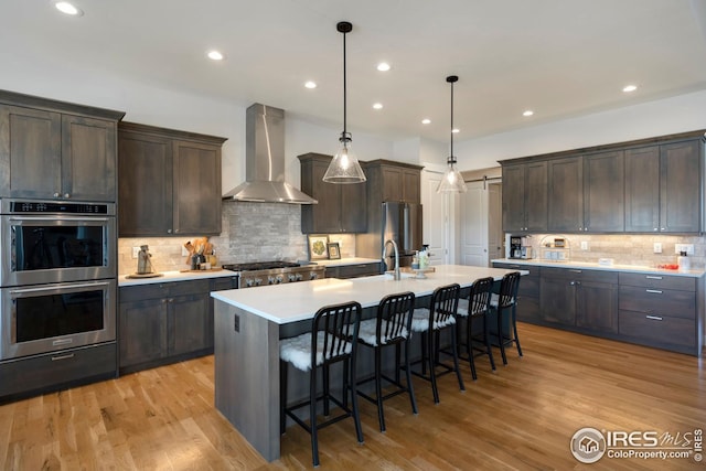 kitchen with a breakfast bar area, stainless steel appliances, dark brown cabinetry, and wall chimney exhaust hood