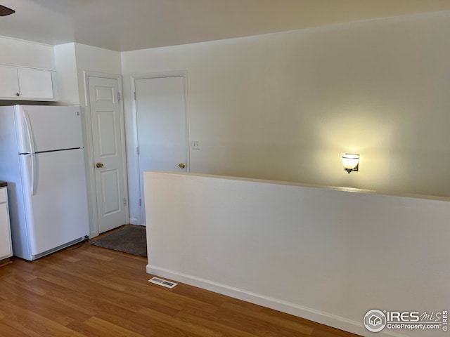 kitchen with white cabinetry, white fridge, and light hardwood / wood-style flooring