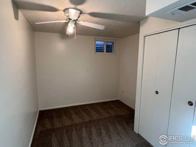 unfurnished bedroom with dark colored carpet, ceiling fan, a textured ceiling, and a closet