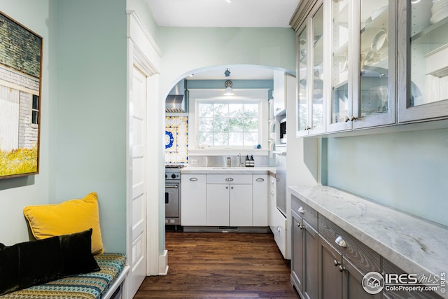 interior space with sink, stainless steel stove, wall chimney range hood, light stone counters, and dark hardwood / wood-style flooring