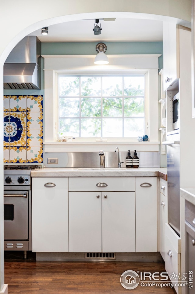 kitchen with dark hardwood / wood-style floors, white cabinetry, sink, gas stove, and wall chimney range hood