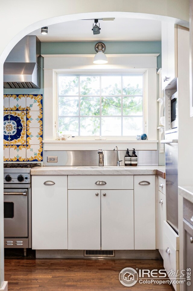 kitchen with wall chimney range hood, light countertops, a sink, stainless steel range, and white cabinets