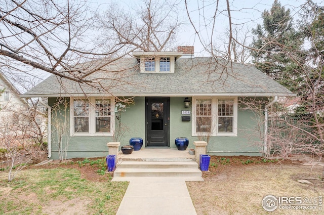 bungalow with a chimney, a shingled roof, and stucco siding