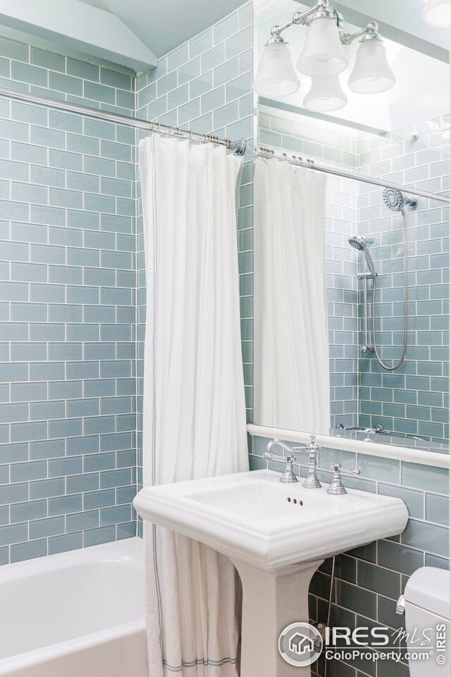 bathroom with a sink, tile walls, toilet, and shower / tub combo