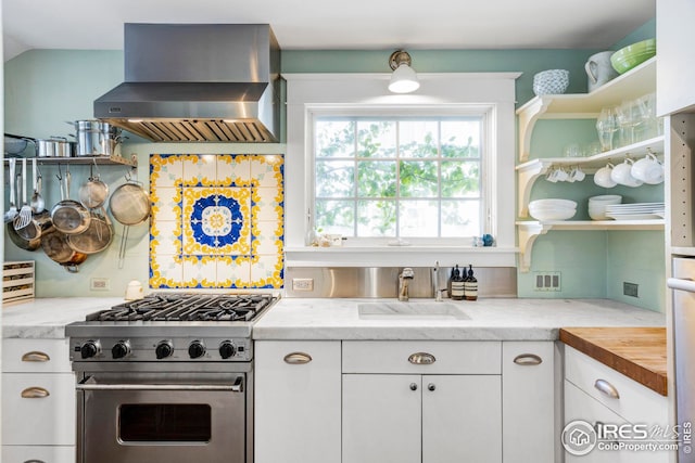 kitchen with ventilation hood, white cabinetry, sink, stainless steel range, and light stone countertops