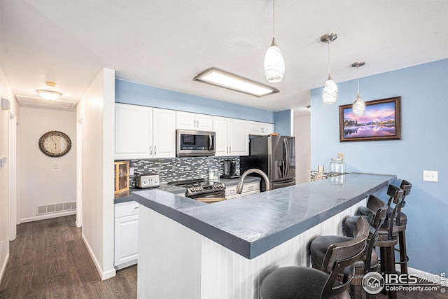 kitchen with white cabinetry, decorative light fixtures, appliances with stainless steel finishes, kitchen peninsula, and backsplash